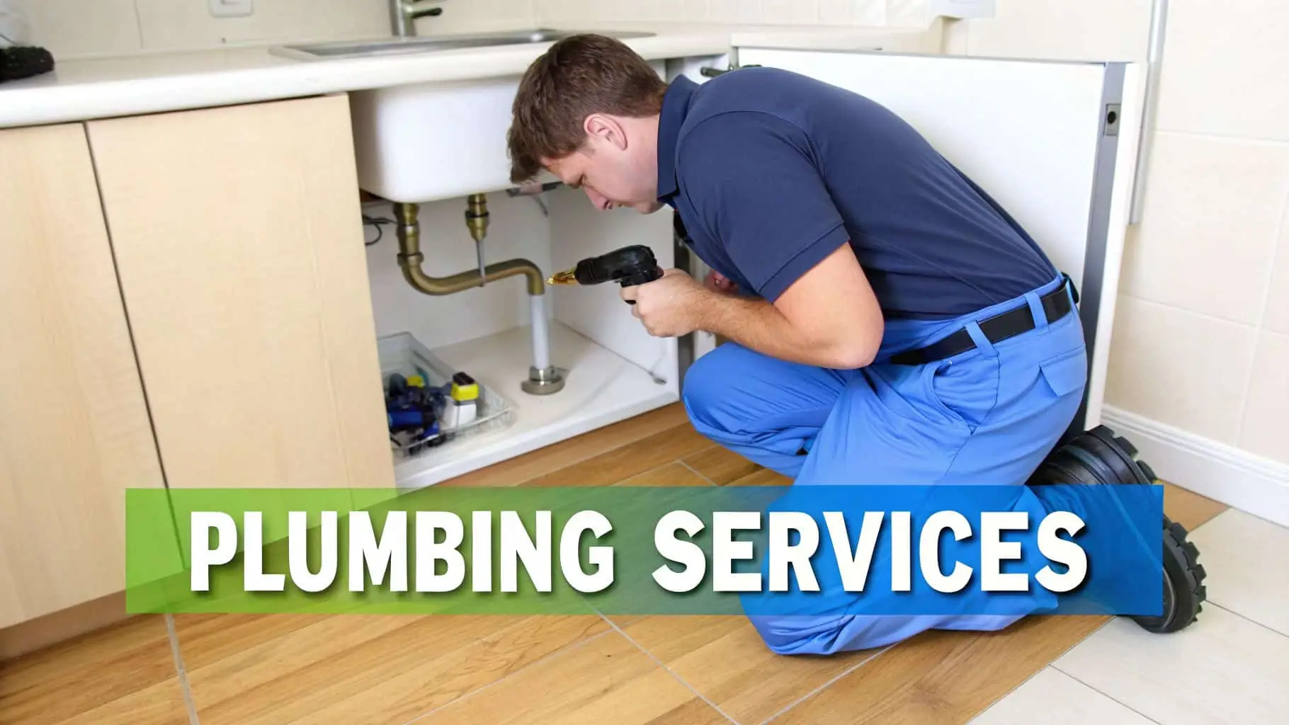 A male plumber in a blue uniform crouches, inspecting the pipes under a kitchen sink with a tool.