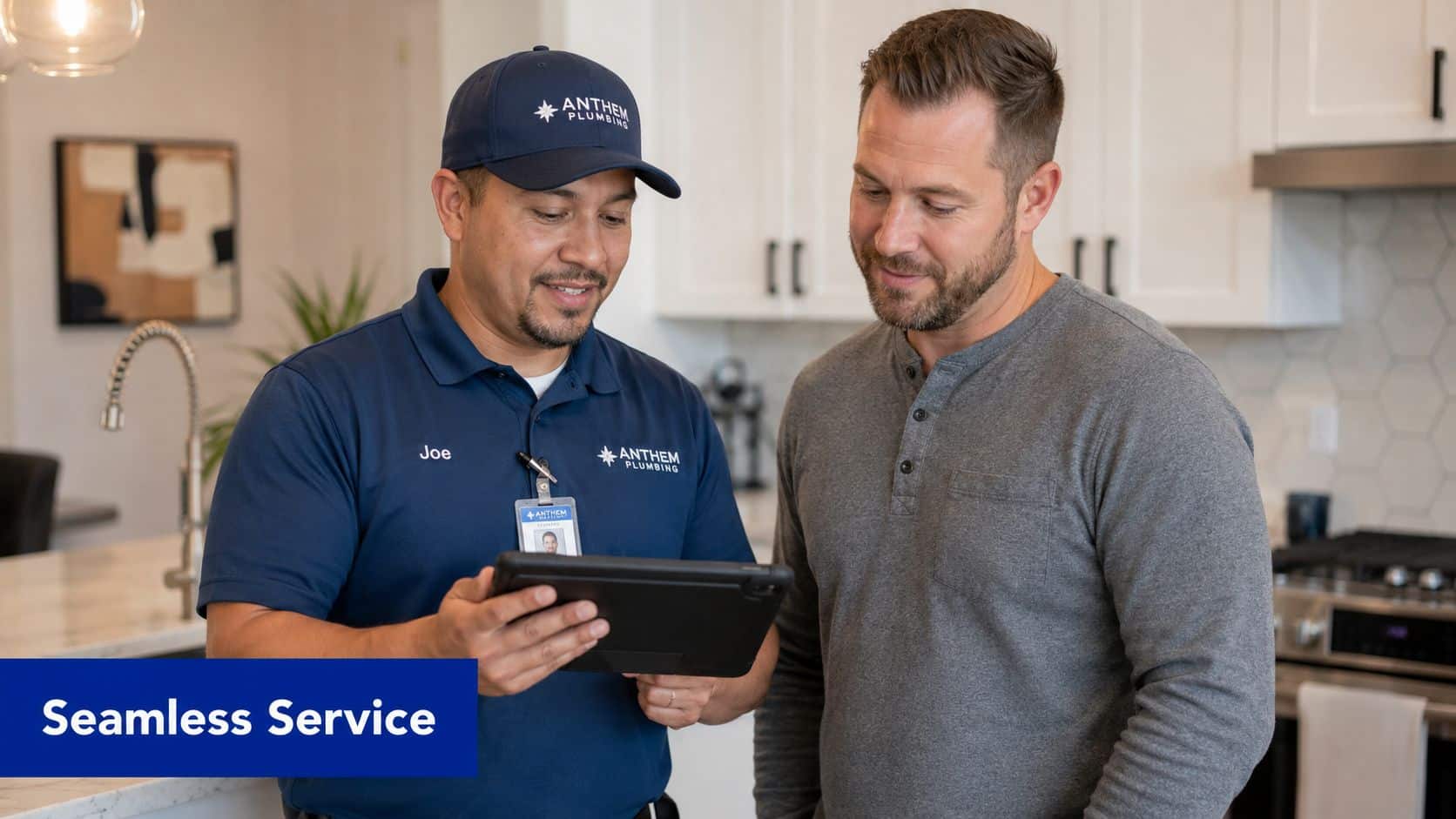 A professional Anthem Plumbing technician explains a service plan on a tablet to a homeowner in a kitchen.