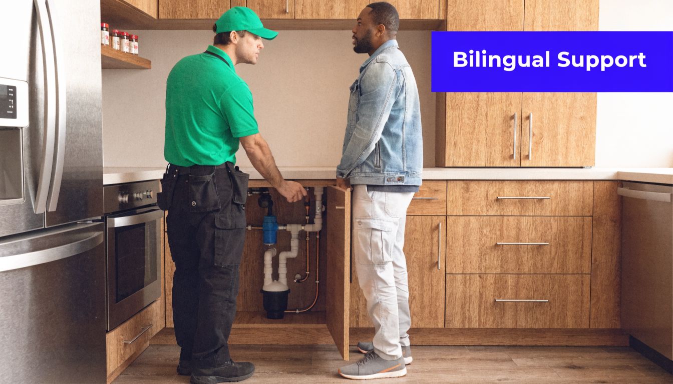 A professional plumber wearing a green uniform consulting with a customer in a modern kitchen.